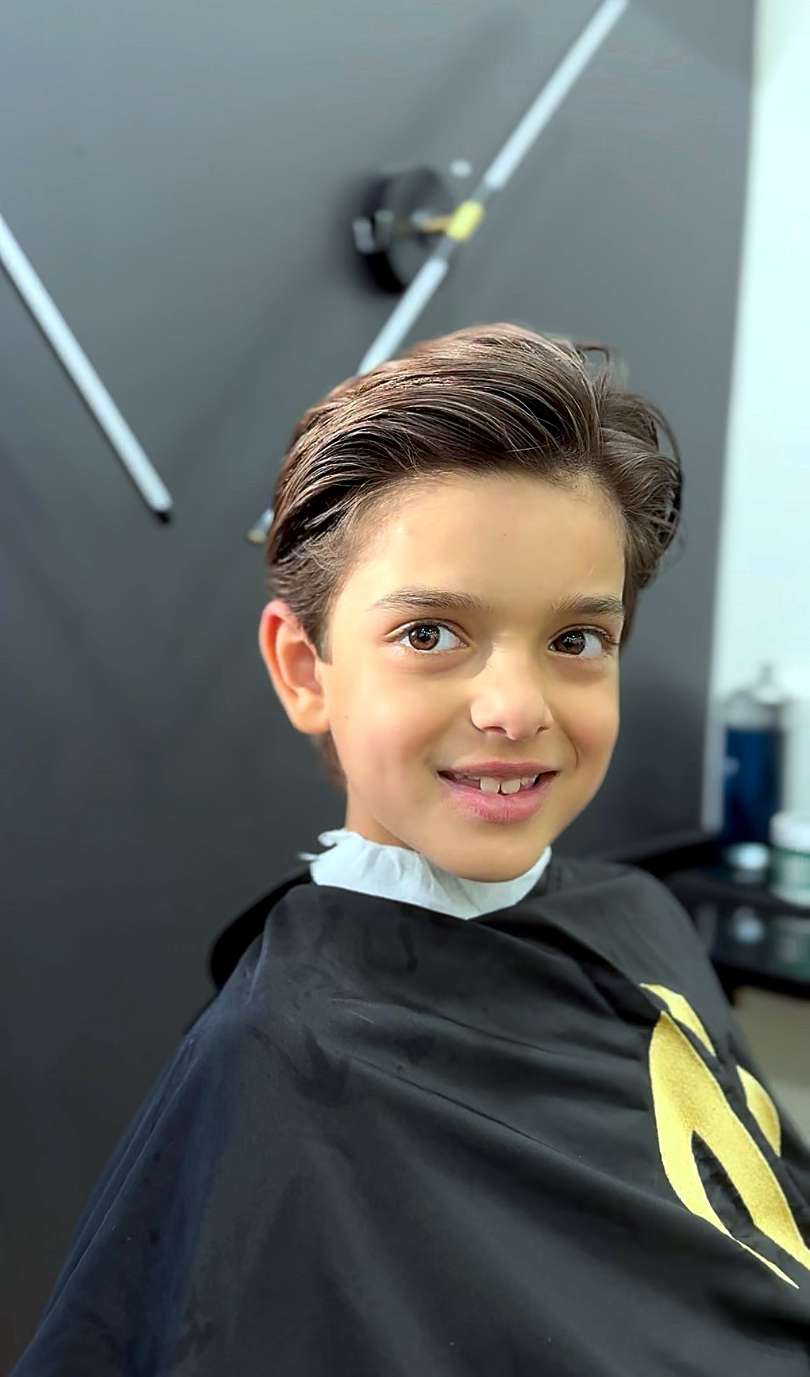 Young boy smiling in a salon cape after a haircut
