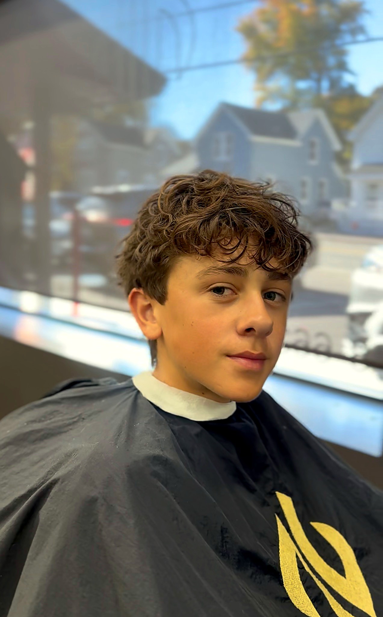 Teen boy with curly hair in a salon cape